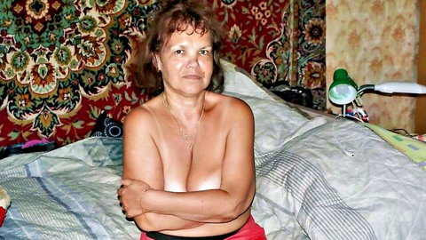 Curly-haired mature granny topless, arms covering large breasts in amateur pose