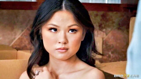 Topless Asian beauty with bare shoulders and perky tits stares at camera amid cardboard boxes
