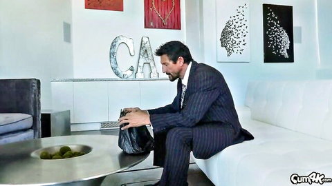 Suited man sitting on white couch holding black purse in luxury living room