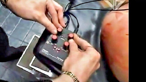 Man's hands grip e-stim controller wired to woman's red spanked bare ass in BDSM punishment