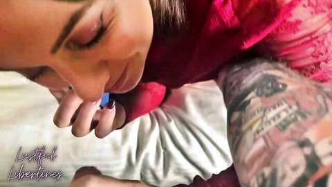 Lustful Libertines in seductive red dress with tattoos, smiling on bed