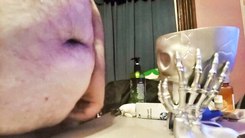 Blurry closeup of bruised gay guy face near silver skeleton hand prop on table solo