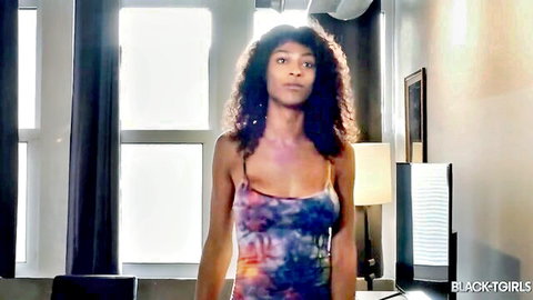 Curly-haired ebony beauty poses seductively in skimpy tie-dye dress flaunting deep cleavage and big tits