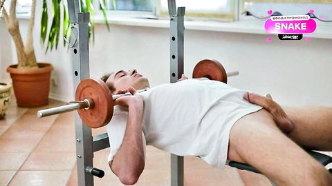 Athletic man trapped under barbell in gym, hand on bulging underwear crotch