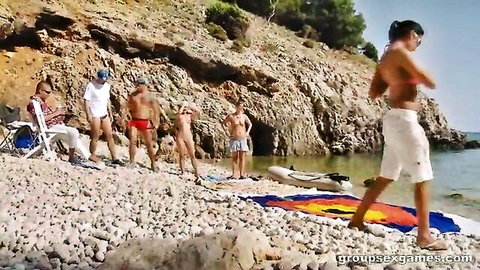 Topless woman in white thong with bulge men in speedos on rocky beach for outdoor group sex