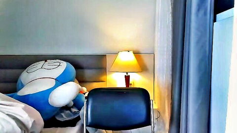 Cozy bedroom corner with large blue Doraemon plush toy on bed beside lit lamp and chair