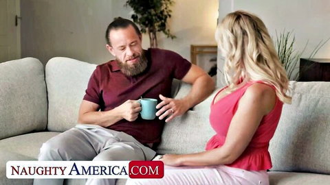 Busty blonde in low-cut pink top shows huge tits cleavage while chatting with bearded guy on couch