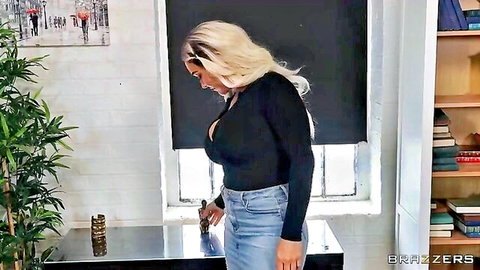 Curvy blonde MILF with huge tits in deep cleavage black top and tight jeans posing in mirror.
