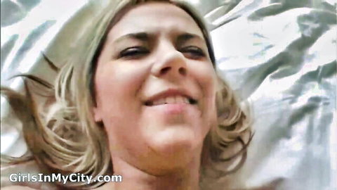 Smiling blonde milf topless on bed, seductive gaze