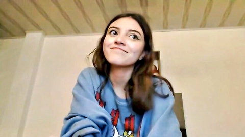 Cute brunette teen in blue sweatshirt smiling, thumbnail for dancing and masturbating video