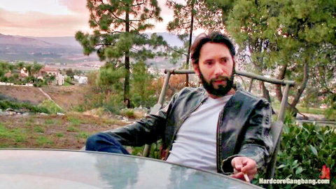 Bearded man in leather jacket smokes outdoors, angry boyfriend in gangbang punishment scene