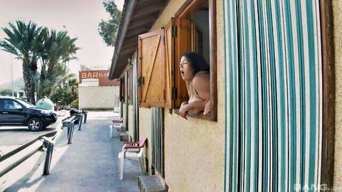 Excited long-haired Asian babe in skimpy bikini top leaning out beach hut window with mouth wide open