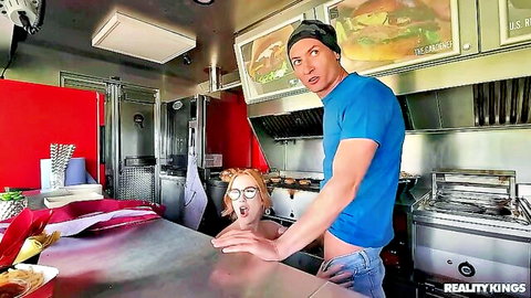 Redhead with glasses kneels for blowjob on guy in food truck kitchen