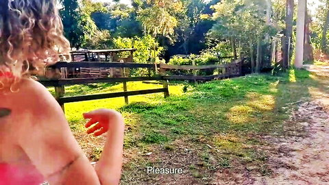 Curly-haired woman in red top exposing shoulder outdoors in woods