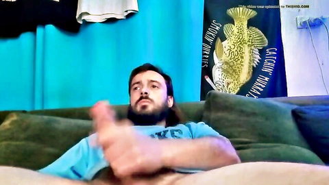 Bearded young man strokes his erect cock with handjob on green living room couch
