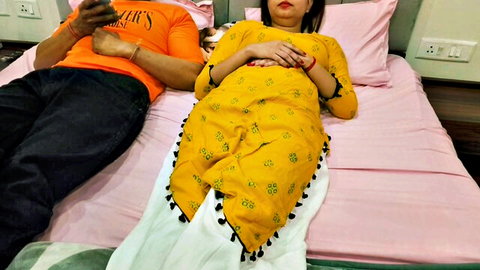 Indian couple in yellow salwar kameez and orange shirt lying clothed on bed