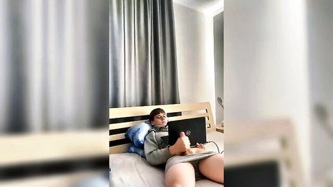 Amateur twink on bed with laptop, hand in crotch area