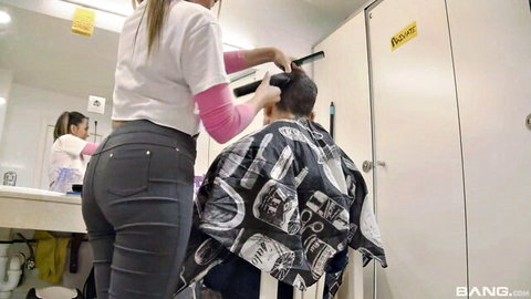 Blonde barber in tight pants trims man's hair, teasing ass view