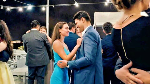 Sexy brunette in tight blue dress dances intimately with handsome suited man at outdoor party under string lights