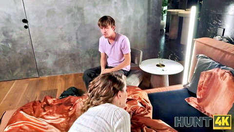 Skinny long-haired brunette on all fours on couch in living room looking back at young guy