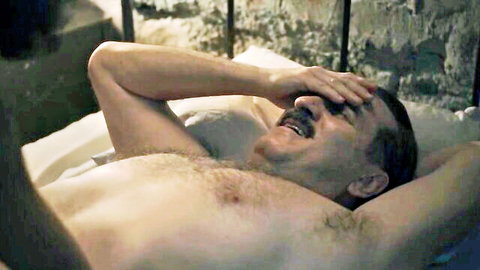 Shirtless man laughing in bed from Yessica Borroto Perryman nude sex scene in The Dead Girls (2025)