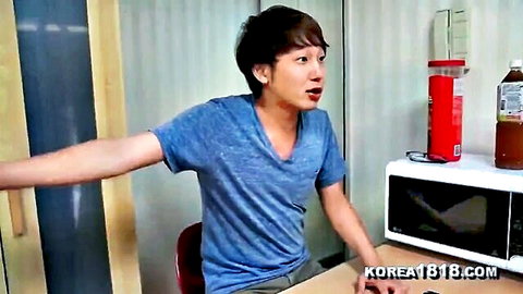 Surprised Korean guy in blue t-shirt leans back with arms outstretched in casual room