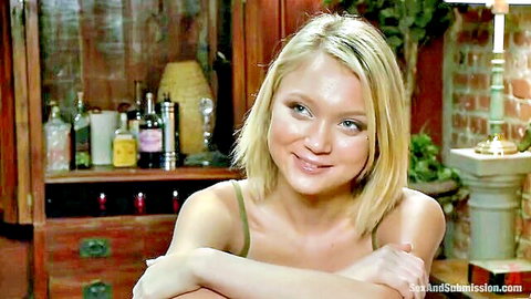 Petite blonde with small tits smiles playfully in thin camisole at home bar