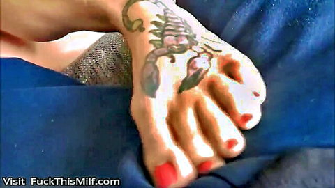 Close-up of sexy MILF's bare feet with scorpion tattoo and red toenails teasing on blue couch