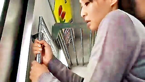 Asian woman in gray top gripping subway rail, checking phone intently
