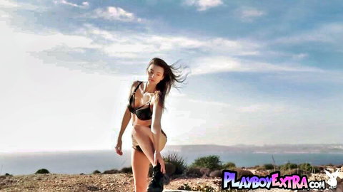 Brunette babe in skimpy leather bikini bends over teasing perfect tits and ass outdoors on ocean cliff