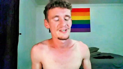 Gaydriano shirtless smiling in bedroom with rainbow flag, athletic build