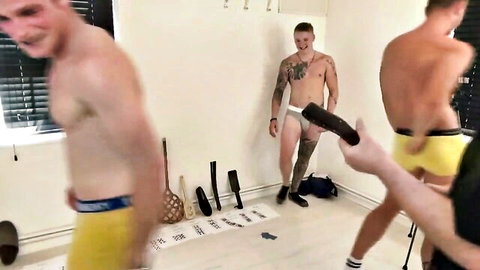 Tattooed muscular gay hunk in tight white briefs holds thick black dildo amid punishment toys and studs in yellow underwear