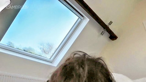 Brunette with messy long hair lying on bed gazing up at skylight in bedroom