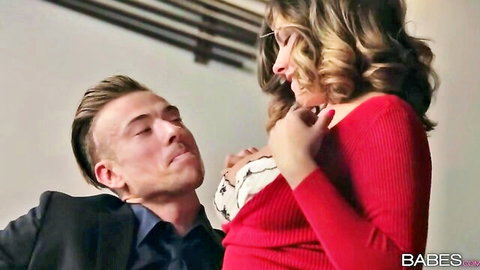Curly-haired woman in red sweater teases cleavage with suited man in office