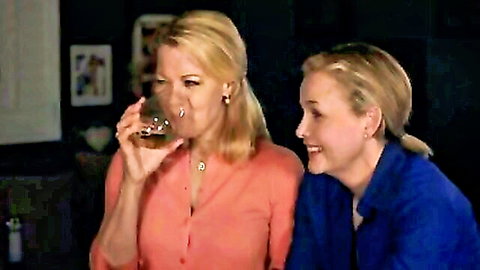 Two blonde MILFs in orange and blue tops sharing drinks and smiles