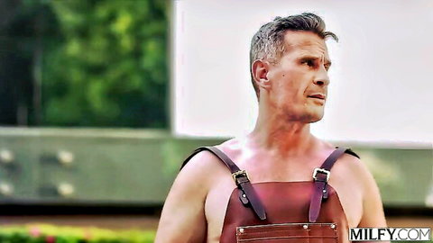 Muscular shirtless man in leather suspenders stands outdoors on MILFY