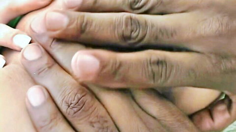 Black hands gripping white woman's manicured fingers passionately in close-up interracial tease