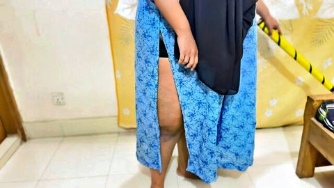 Curvy Indonesian MILF teases thick thighs in high-slit blue sarong holding yellow broom