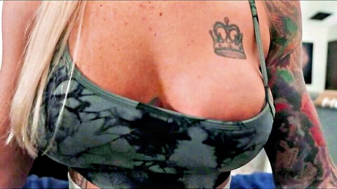 Deliah Grace busty blonde milf in low-cut tie-dye top showing deep cleavage and crown tattoo