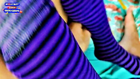 Closeup of sexy legs and feet in purple striped stockings teasing on bed