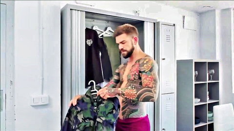 Tattooed muscular hunk in tight pink briefs grabbing camo jacket in locker room