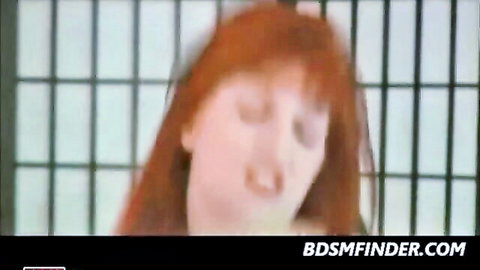 Redhead in prison bars, grimacing in BDSM flogging scene