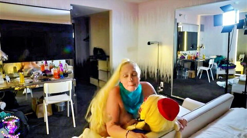 Topless blonde MILF with huge tits cuddles yellow mascot on bed