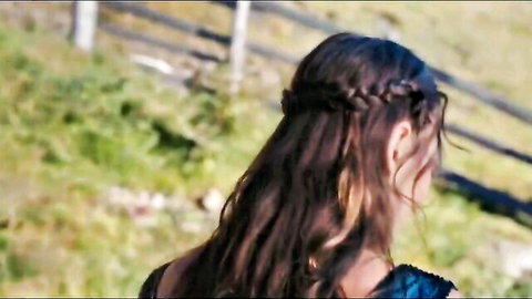Brunette with long braided hair in revealing blue dress showing bare back outdoors near fence