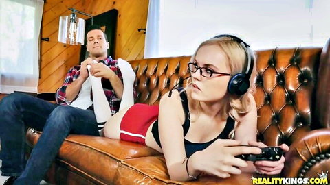 Blonde gamer girl with glasses in knee socks and shorts plays Xbox on couch with boyfriend