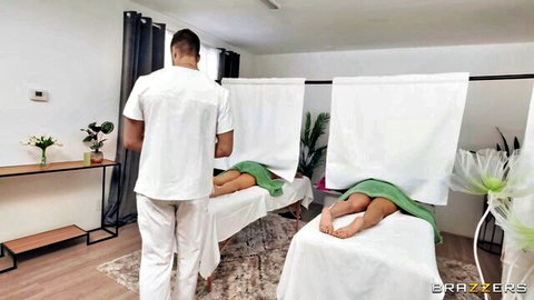 Masseur in white uniform stands between two green towel-covered women on massage tables in spa room