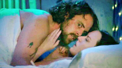 Bearded hunk intimately embraces brunette beauty in bed under sheets with bare chests