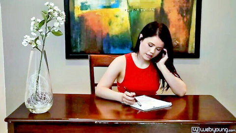 Brunette woman in red dress on phone call, writing at desk