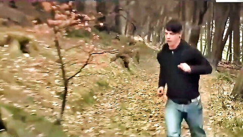 Athletic young man jogging through autumn forest trail looking back over shoulder
