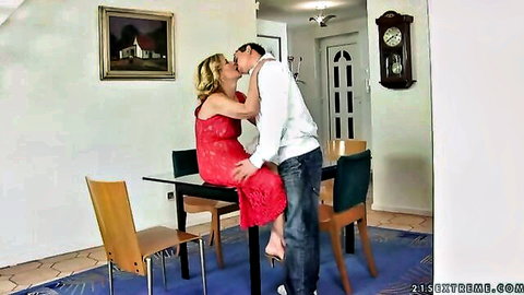 Mature blonde woman in red dress kissing young man passionately